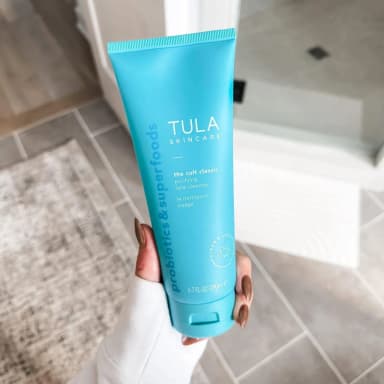 A hand holding a turquoise tube of TULA Skincare The Cult Classic purifying face cleanser